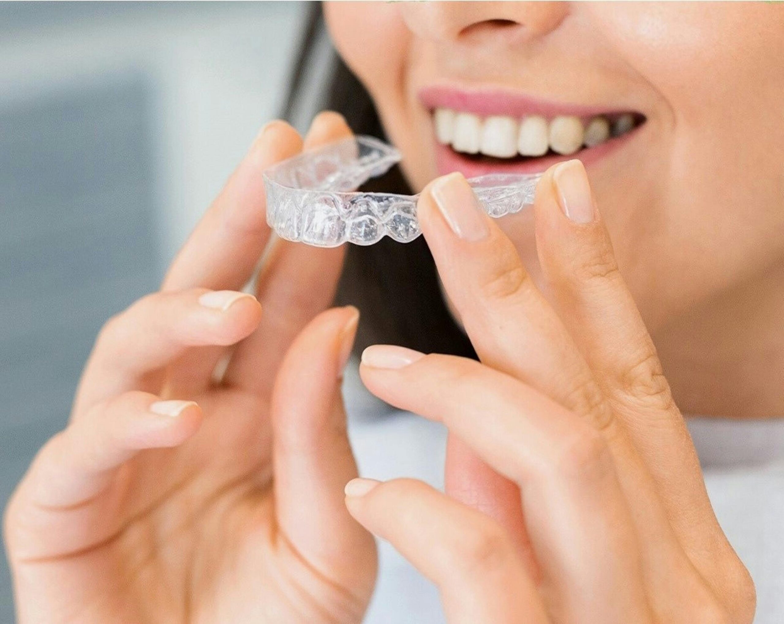 person smiling while holding a clear plastic dental aligner